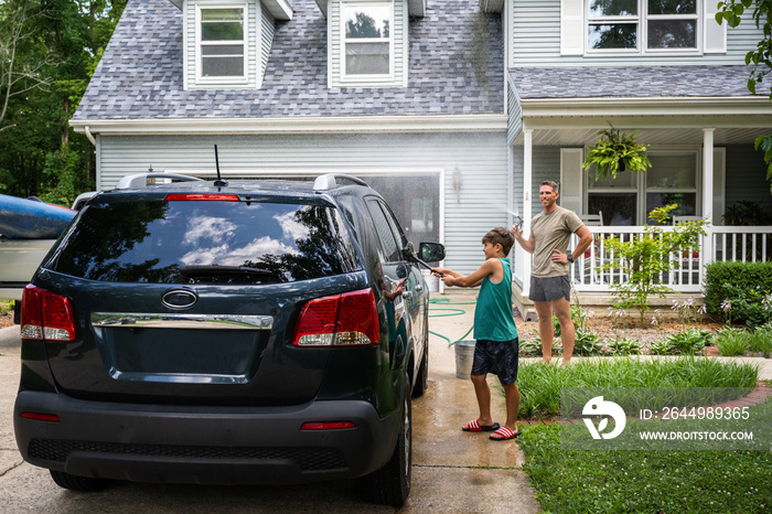 Air Force service member washes his vehicles with his sons in the driveway.