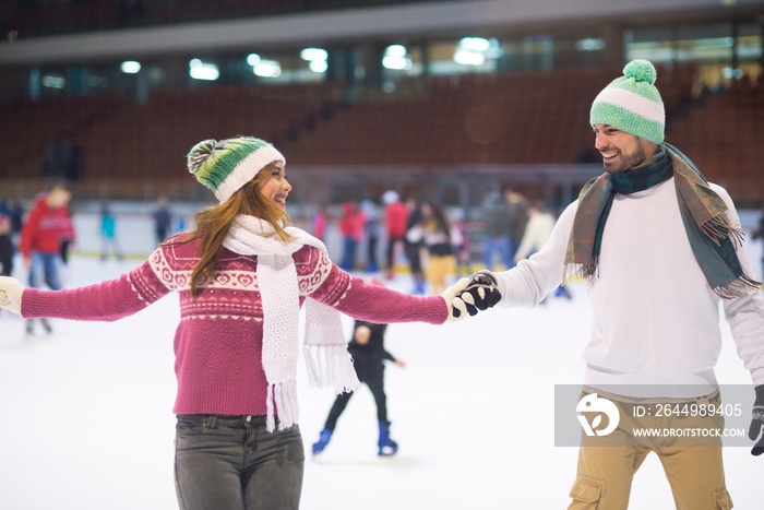 Young smiling couple ice skating in the ice rink in winter