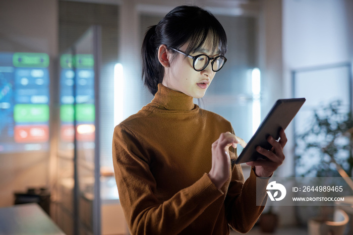 Asian young businesswoman in eyeglasses using digital tablet to work online while standing at office