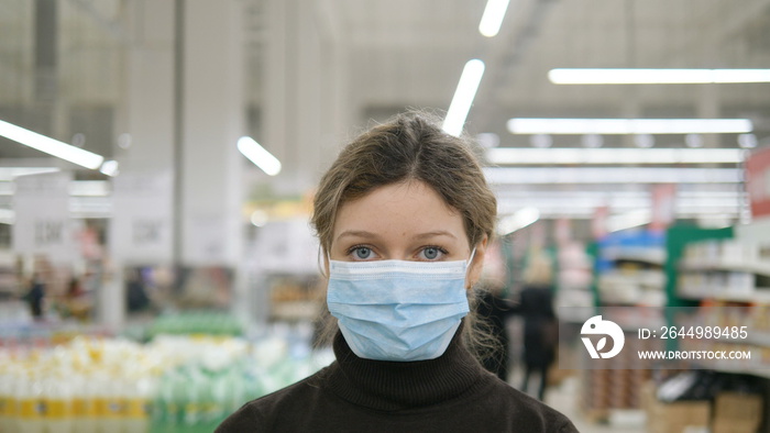 A young woman puts on a medical mask in a grocery supermarket close up