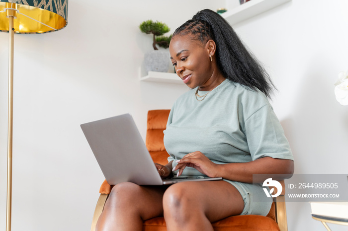 Young woman using laptop while sitting in armchair at home