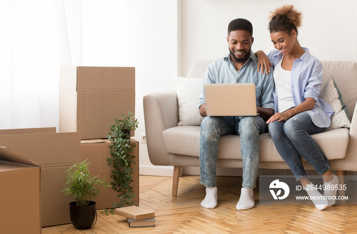 Joyful Couple Using Laptop Sitting On Sofa In New House