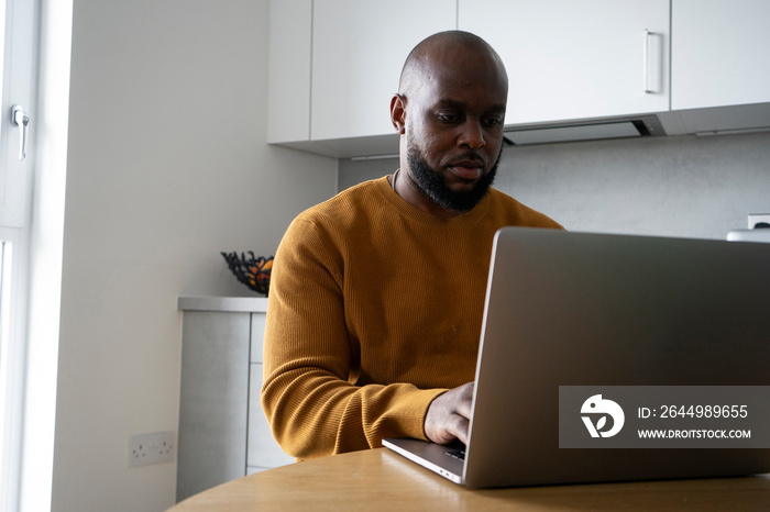 Man using laptop at table in kitchen