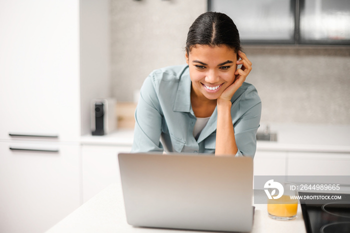 Smiling and concentrated businesswoman in casual wear is looking at the laptop screen, solving tasks, freelance woman working remotely from home