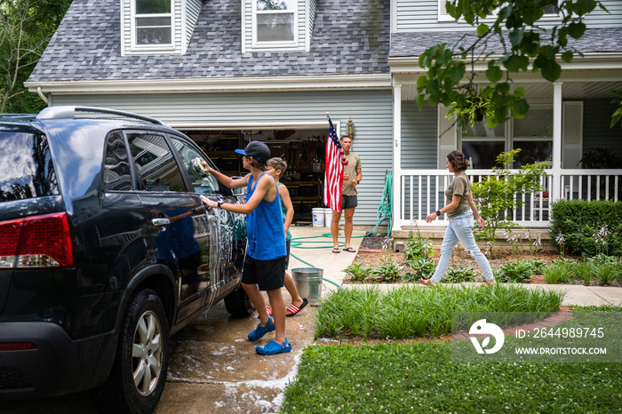 Air Force service member washes his vehicles with his sons in the driveway.