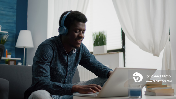 Black african american man wearing headphone, typing on laptop, using internet web online services. Remote working from home computer user using modern technology and communication devices