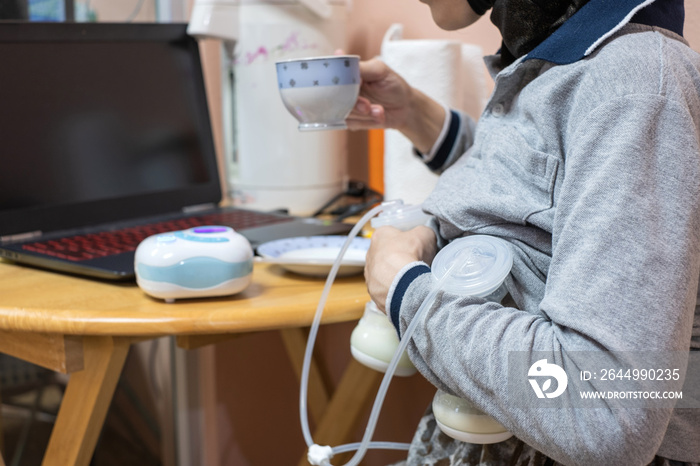 Busy mother pumping breastmilk with automatic breast pump machine while drinking coffee.