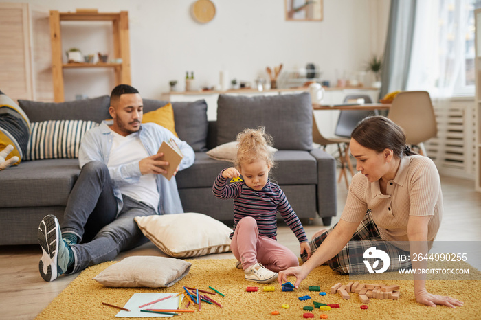 Full length portrait of modern mixed-race family playing with cute little girl in cozy living room interior, copy space