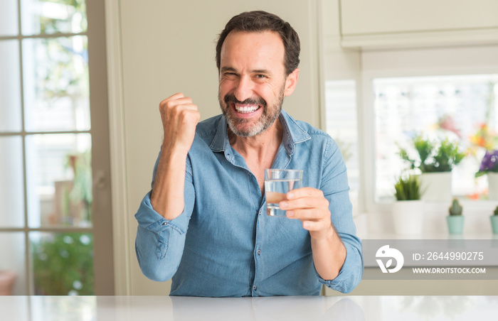 Middle age man drinking a glass of water screaming proud and celebrating victory and success very excited, cheering emotion