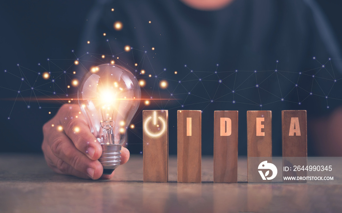 Start new idea with innovation and inspiration concept, Hand holding light bulb and word IDEA on wood block, new idea, start-up of business, Innovative technology in science and network communication.