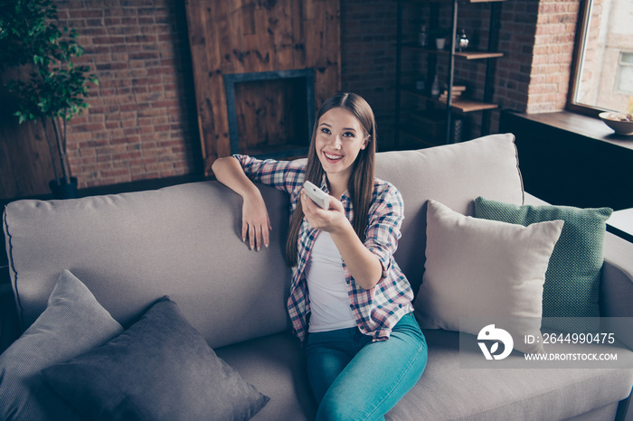 Pretty satisfied cheerful she her lady using remote controller for changing temperature in interior loft room relaxing on beige divan