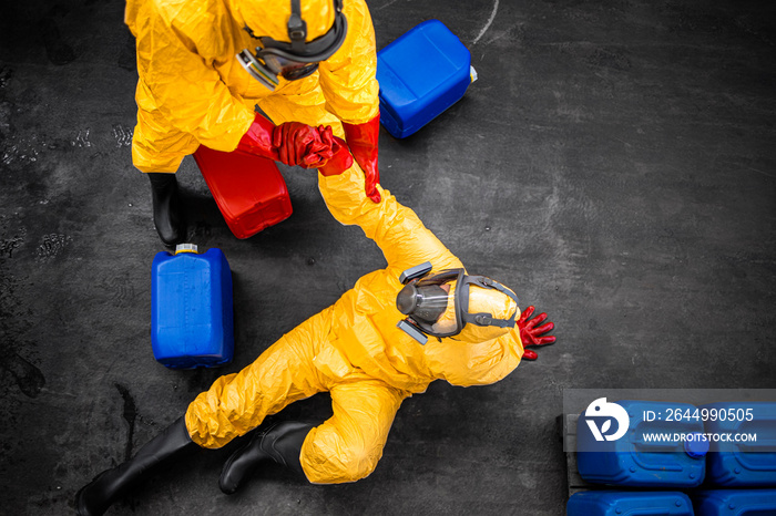 Chemicals worker in protection suit helping his coworker to stand up after falling down. Accident at work.