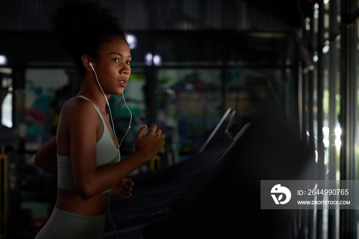 young sports woman working out with wired earbuds and running on treadmill in gym