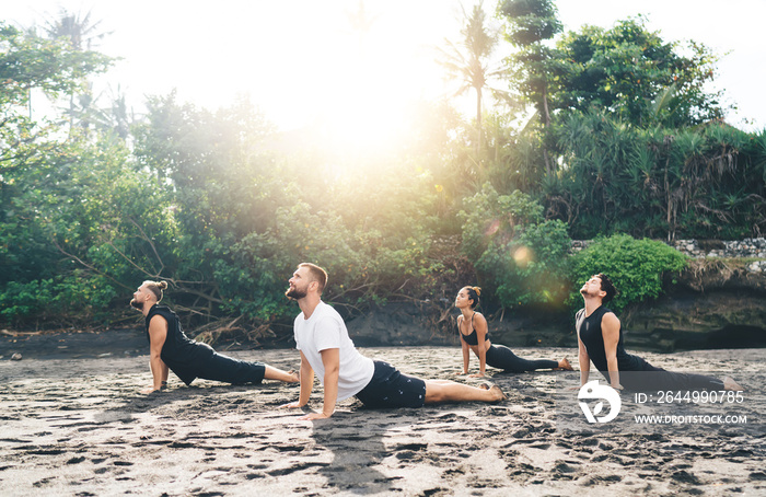 Group of male and female in active wear enjoying recreation during yoga activity at coastline in Bali, people doing stretching asana reaching health and balance during morning aerobic training