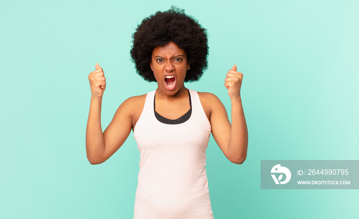 black afro woman shouting aggressively with an angry expression or with fists clenched celebrating success