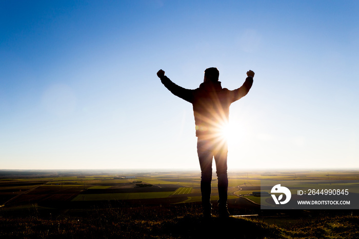 silhouette of a man at sunset raising his arms. Concept of achievement and victory