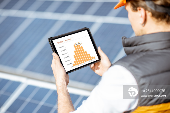 Man examining genaration of solar power plant, holding digital tablet with a chart of electricity production. Concept of online monitoring of the electric station