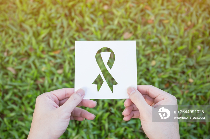 Hands holding cut paper with logo of ribbon over green glass background. Symbol icon for breast cancer awareness. Healthcare and medical spring concept banner