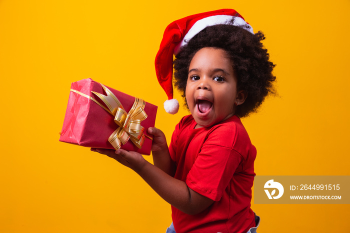 Smiling afro child in Santa Claus red hat holding christmas gift in hand. Christmas concept.