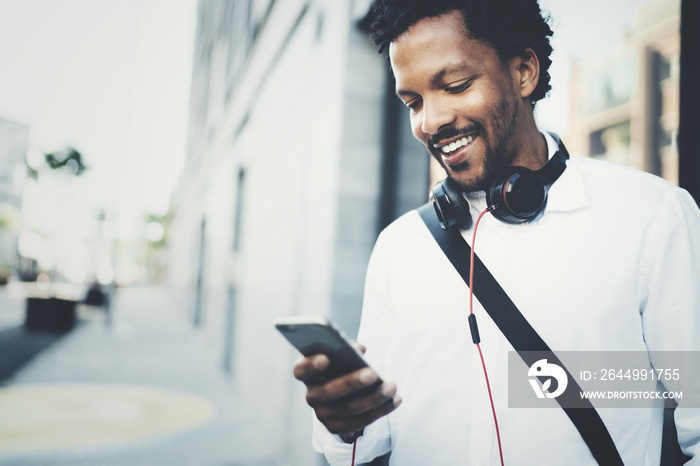 Closeup view of Happy smiling African man using smartphone outdoor.Portrait of young black cheerful man texting a sms message with friends.Blurred background.