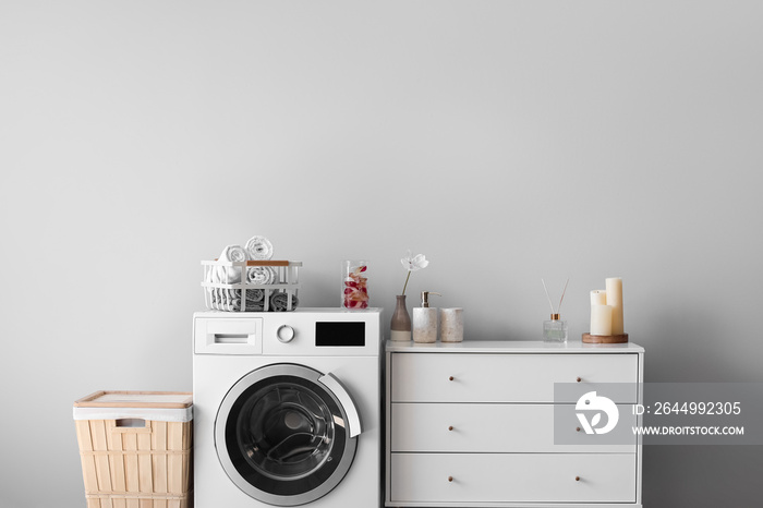 Interior of light laundry room with washing machine, basket and chest of drawers