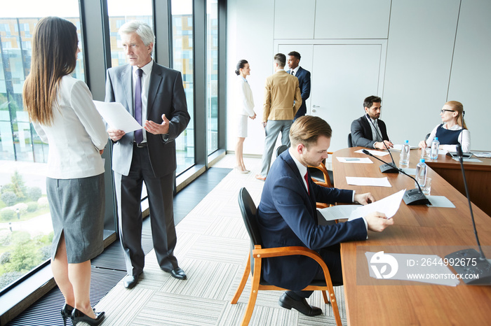 Modern successful business people talking and discussing agenda before beginning of meeting in business conference room