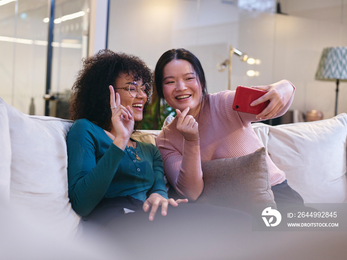 UK, London, Two female coworkers taking selfie in modern office lobby