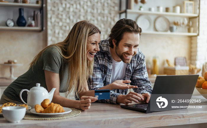 Smiling millennial caucasian man with stubble and lady with credit card shopping online on laptop