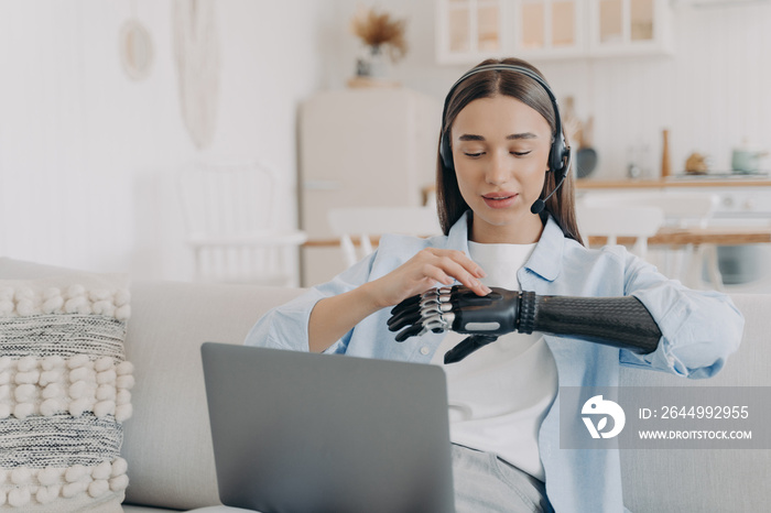 Girl with disability in headset customizes bionic prosthetic at laptop. Lifestyle of disabled people