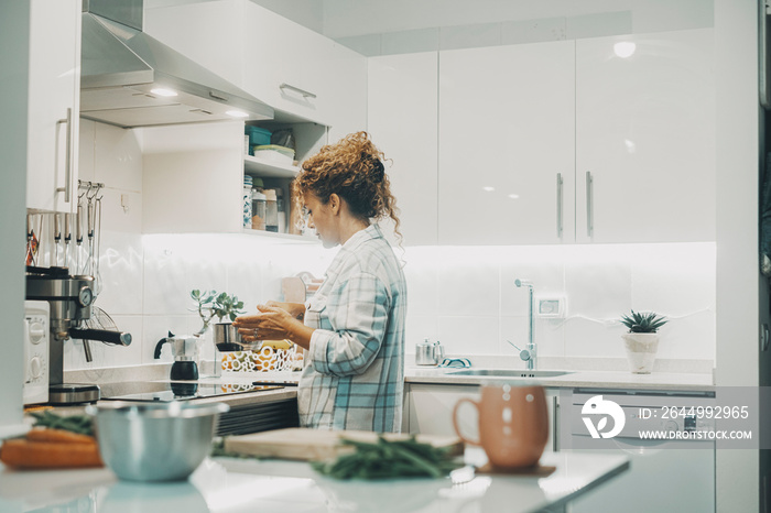 One woman cooking at home in the kitchen alone. Real single lifestyle for independent female people. Housewife preparing lunch for the family. View of lady using pot and prepare food indoor life.