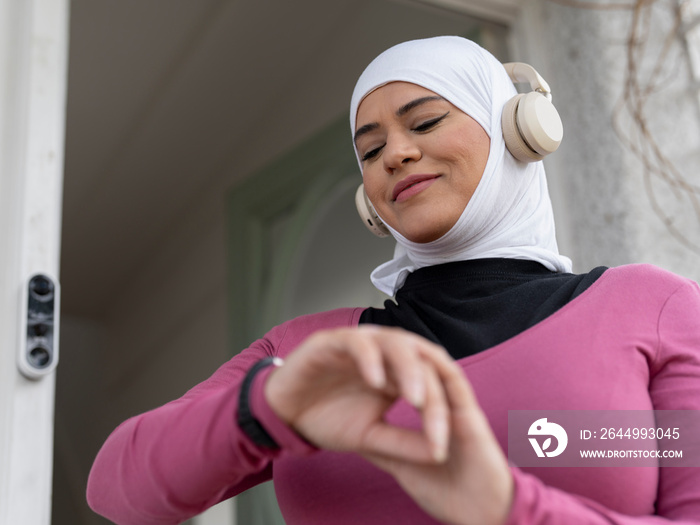 UK,Sutton,Woman in headscarf and headphones checking smart watch