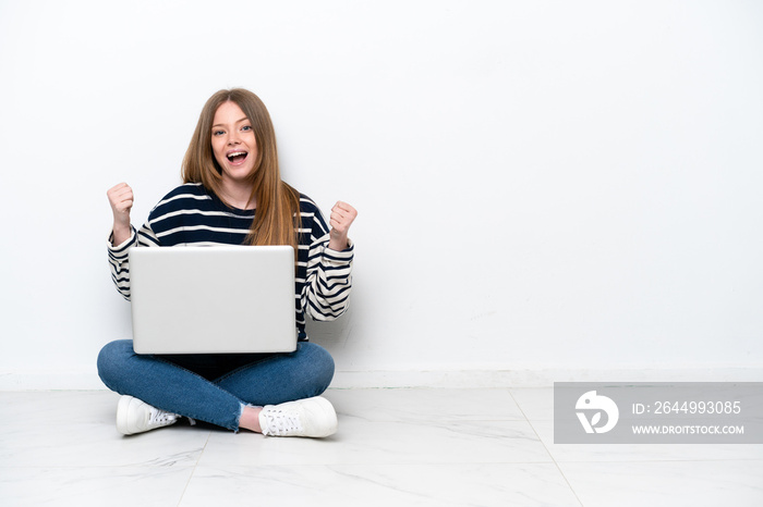 Young caucasian woman with a laptop sitting on the floor isolated on white background celebrating a victory in winner position