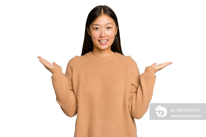 Young Asian woman isolated on green chroma background makes scale with arms, feels happy and confident.