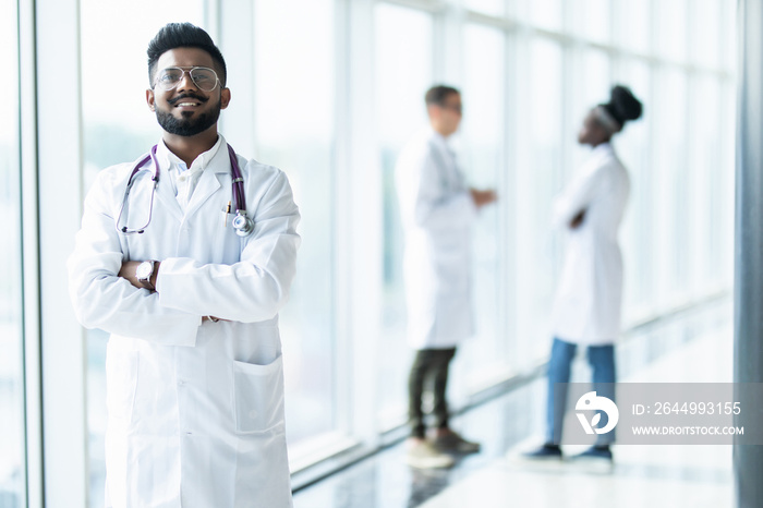 Young indian male doctor in white uniform with collegues on the background