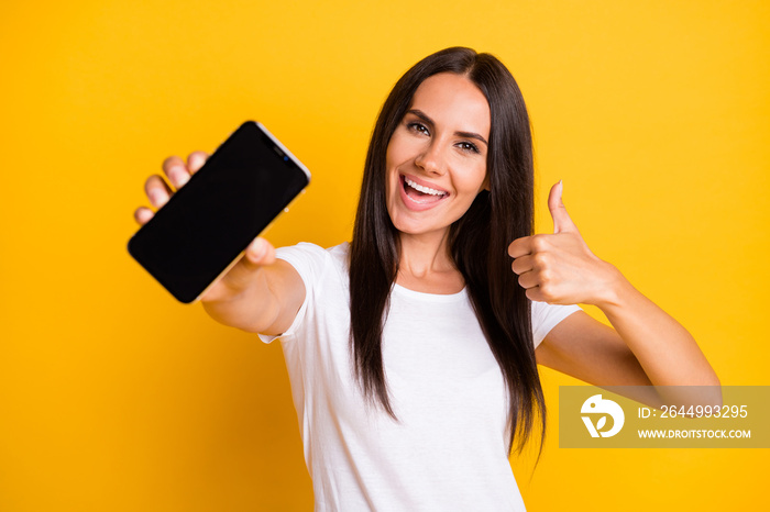 Photo portrait of young girl showing mobile phone touchscreen empty space showing like sign isolated on vivid yellow color background