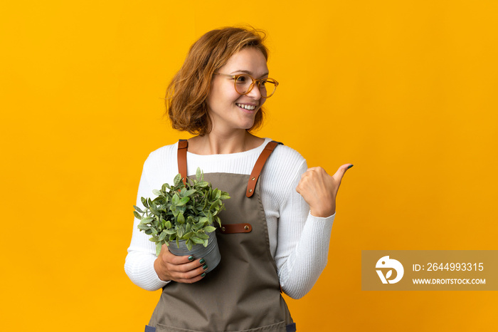 Young Georgian woman holding a plant isolated on yellow background pointing to the side to present a product