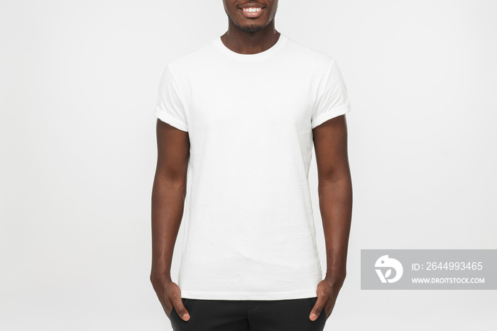 Young african american man standing with hands in pockets, wearing blank white t shirt with copy space for your logo or text, isolated on grey background