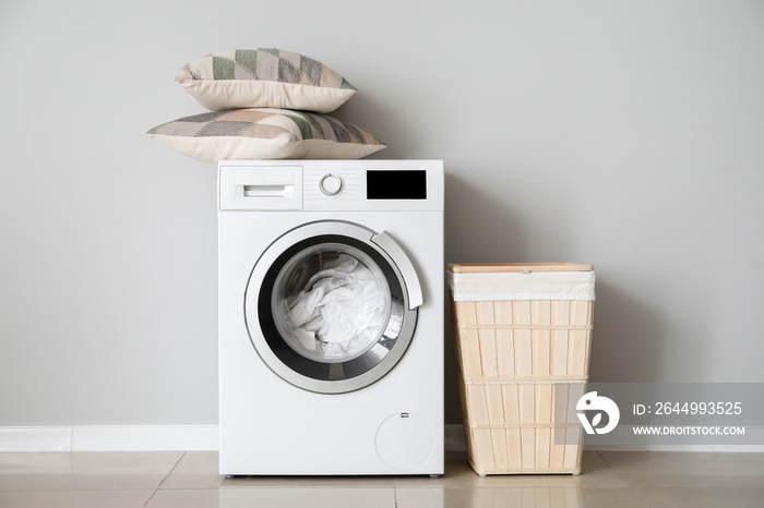 Modern washing machine with laundry near white wall