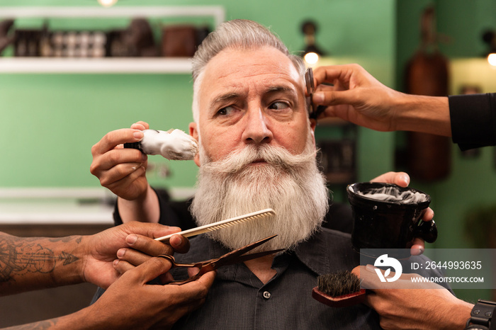 an older man with a white beard is shaved, combed, hair cut by several hands of hairdressers and barbers. barbering tools