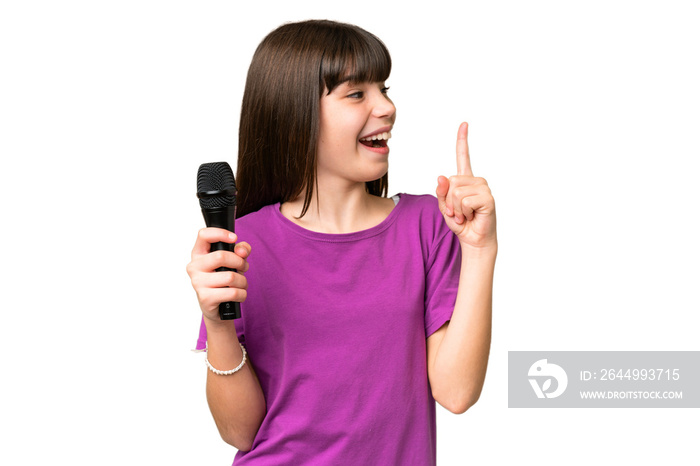 Little singer girl picking up a microphone over isolated background intending to realizes the solution while lifting a finger up