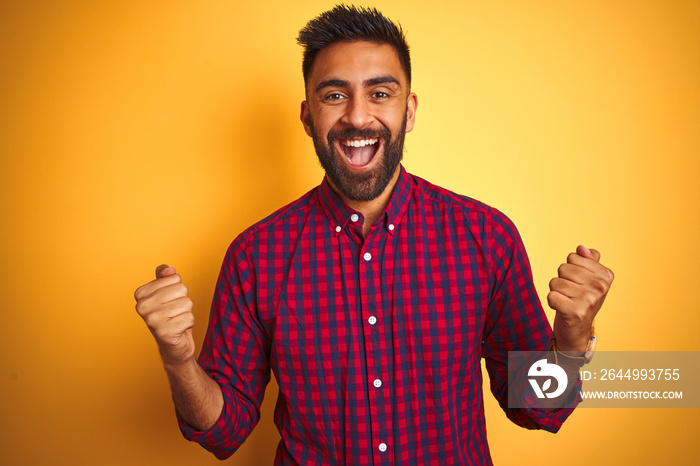 Young indian man wearing casual shirt standing over isolated yellow background celebrating surprised and amazed for success with arms raised and open eyes. Winner concept.