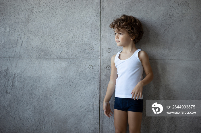 Profile portrait of a handsome little boy in underwear posing on concrete wall, looking a one side, copy space.