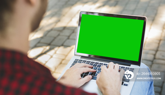 Millennial man typing on laptop with green screen