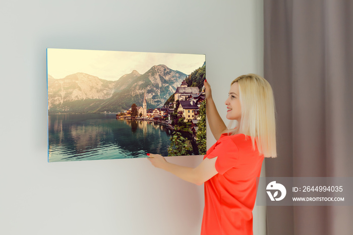 A happy young blonde woman is holding a large wall photo canvas at home