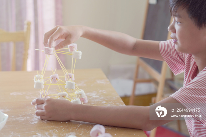 Mixed race Asian preteen boy building tower with spaghetti and marshmallow learning remotely at home, STEM science, homeschooling education, Social distancing, montessori concept