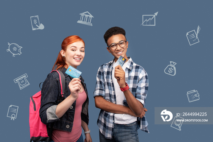 Credit cards. Cheerful smiling students feeling confident while standing together after getting their first credit cards in a reliable bank