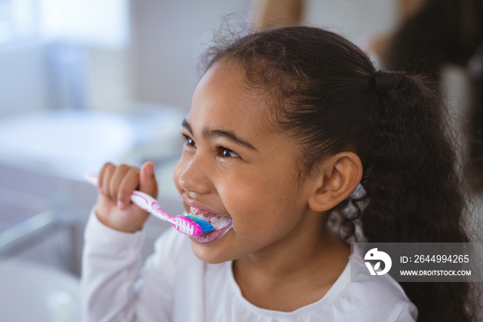 Cute biracial girl brushing teeth while looking away in bathroom