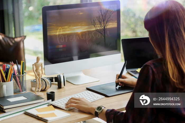 Young hipster graphic designer woman using digital graphic tablet while working at modern office, professional female retoucher sitting at modern workspace with wooden table