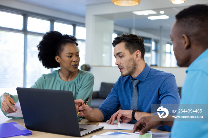 Diverse business people using laptop and discussing in modern office