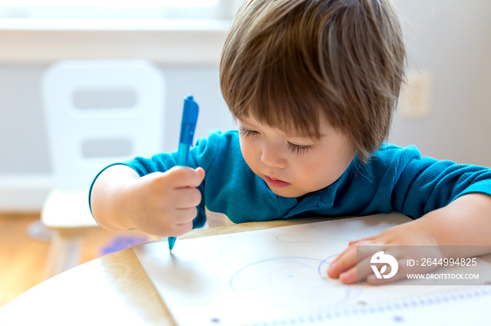 Toddler boy drawing with pen and paper at his desk